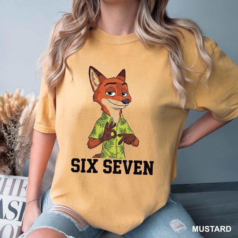 May include: Mustard-coloured t-shirt with a cartoon fox in a green Hawaiian shirt, giving an 'okay' hand sign. The words "SIX SEVEN" are printed in bold black letters. The shirt is a casual wear item, perfect for everyday wear.
