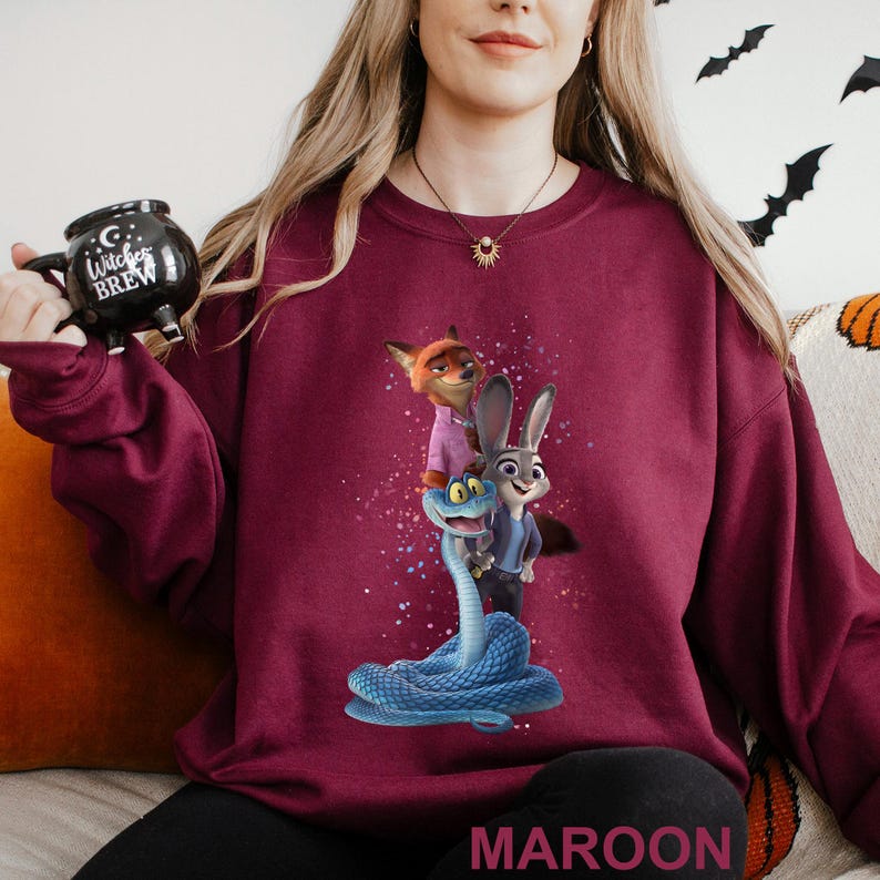 Puede incluir: Sudadera granate con un gr&aacute;fico colorido de personajes de dibujos animados. El dise&ntilde;o incluye un zorro, un conejo y una serpiente azul. La palabra "MAROON" est&aacute; impresa en la parte inferior.