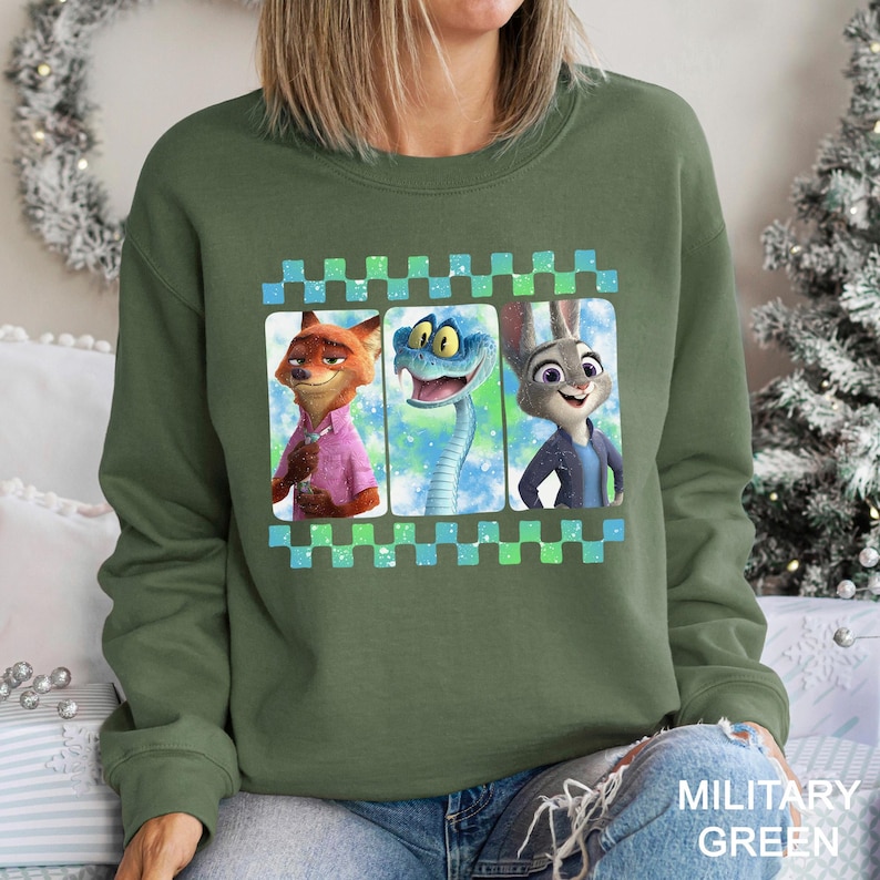 May include: Military green sweatshirt featuring a graphic of three cartoon characters: a fox, a snake, and a rabbit. The characters are in a checkered frame with blue and green squares. The sweatshirt is a solid military green color.