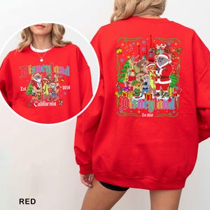 May include: A red Disneyland sweatshirt with a colorful graphic on the front and back. The front graphic includes the Disneyland logo, Santa Claus, and various cartoon characters. The back graphic features the Disneyland logo, Santa Claus, and other cartoon characters.