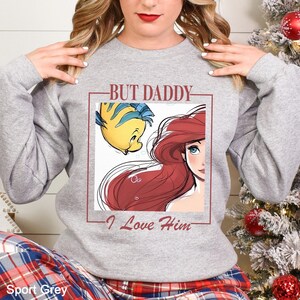 May include: Light grey sweatshirt with a graphic of Ariel and Flounder from The Little Mermaid, and the text "BUT DADDY - I Love Him". The sweatshirt is a sport grey colour.
