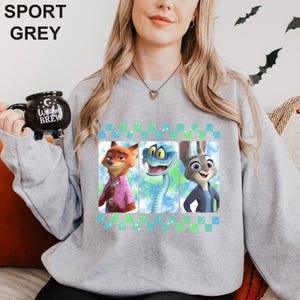 May include: Sport grey sweatshirt featuring three cartoon characters in individual panels. The characters are a fox, a snake, and a rabbit. The sweatshirt has a green and blue checkered design at the top and the words "SPORT GREY" in the upper left corner.
