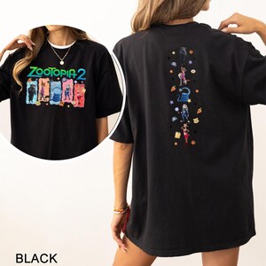 Op de afbeelding: Zwart Zootopia 2 grafisch t-shirt. De voorkant toont "Zootopia 2" boven cartoonfiguren. De achterkant heeft een verticaal ontwerp van Zootopia-personages en iconen. Het shirt heeft een casual, oversized pasvorm.
