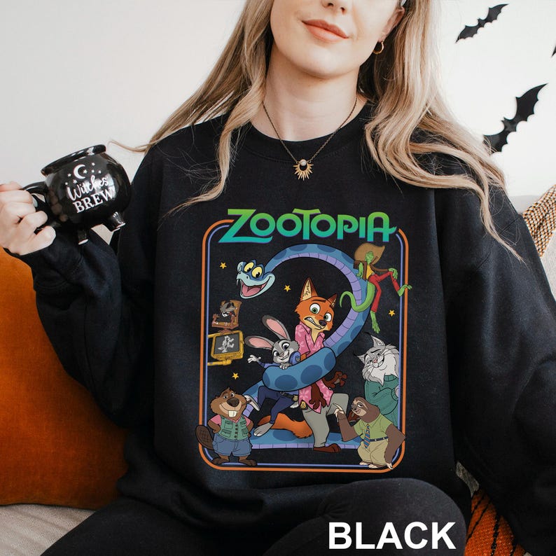 May include: Black sweatshirt featuring a colorful graphic from the animated film Zootopia. The design includes characters like Judy Hopps, Nick Wilde, and others, with the word "Zootopia" in a retro font. The word "BLACK" is printed at the bottom.