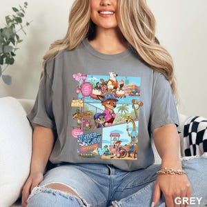 May include: A charcoal gray short-sleeve t-shirt featuring a multi-panel graphic print of animated animal characters in a theme park setting. The design includes various scenes with a fox, a rabbit, and a polar bear, with the text Undercover Mission.