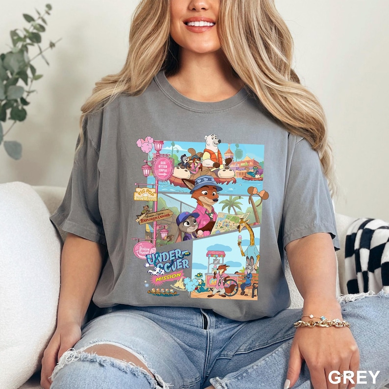 May include: A charcoal gray short-sleeve t-shirt featuring a multi-panel graphic print of animated animal characters in a theme park setting. The design includes various scenes with a fox, a rabbit, and a polar bear, with the text Undercover Mission.