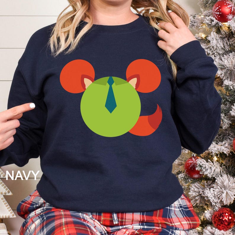 May include: Navy blue sweatshirt featuring a cartoon design of a green circle with a blue tie, red ears, and a red tail. The word "NAVY" is printed in white on the left side of the image. The sweatshirt is part of a holiday-themed collection.