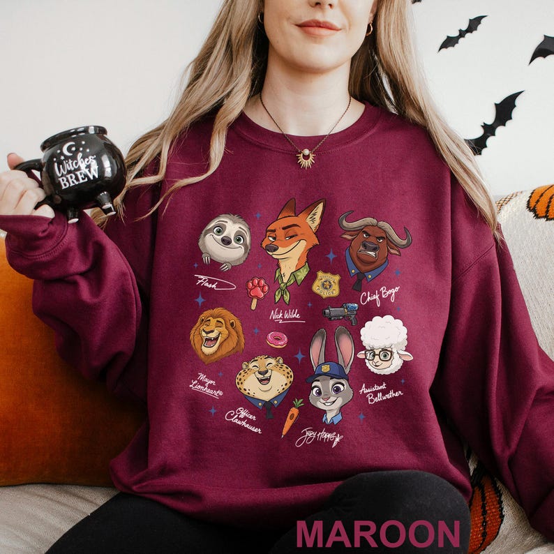 K&ouml;nnte beinhalten: Burgunderfarbenes Sweatshirt mit Zeichentrickfiguren aus Zootopia. Das Design umfasst Flash, Nick Wilde, Chief Bogo, Mayor Lionheart, Officer Clawhauser, Judy Hopps und Assistant Bellwether. Das Wort "MAROON" ist unten aufgedruckt.