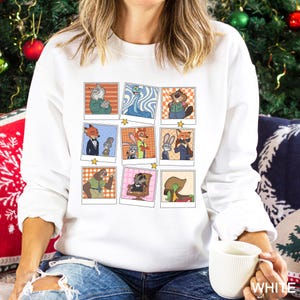 May include: White sweatshirt featuring a grid of cartoon character portraits in retro photo frames. The portraits include a fox, rabbit, and other animal characters. The sweatshirt is a long-sleeved crew neck.