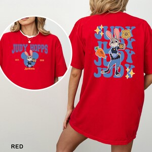 Op de afbeelding: Een rood t-shirt met een afbeelding van Judy Hopps uit Zootopia. De voorkant toont de tekst Judy Hopps, Est. 2016, en een kleine illustratie van het personage. De achterkant toont een grote afbeelding van Judy Hopps, een wortel en een politiebadge.