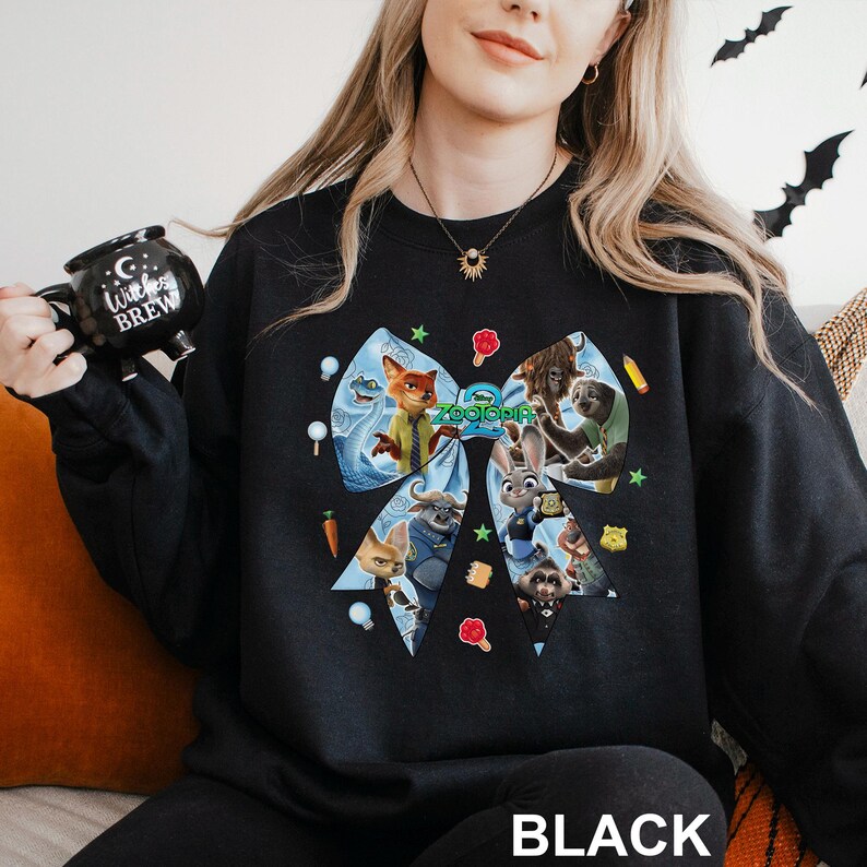 May include: Black sweatshirt featuring a large bow design with characters from the animated film "Zootopia." The bow is light blue with cartoon images of the characters. The word "BLACK" is printed at the bottom of the sweatshirt.