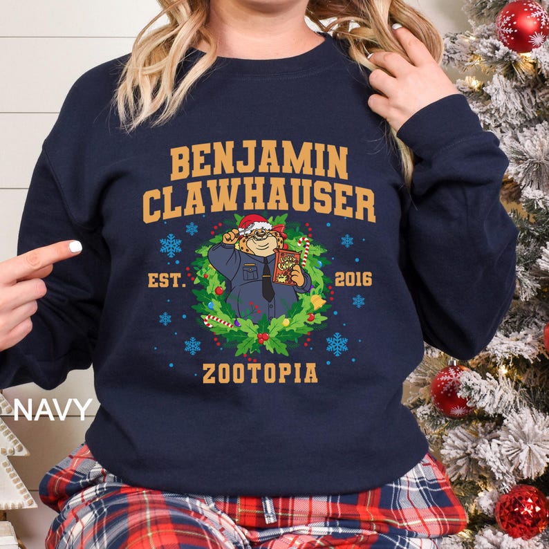 Pu&ograve; includere: Felpa blu navy con il nome "Benjamin Clawhauser" in lettere dorate. Il design include un'immagine a cartoni animati del personaggio di Zootopia, una ghirlanda natalizia, fiocchi di neve e il testo "Zootopia" e "2016".