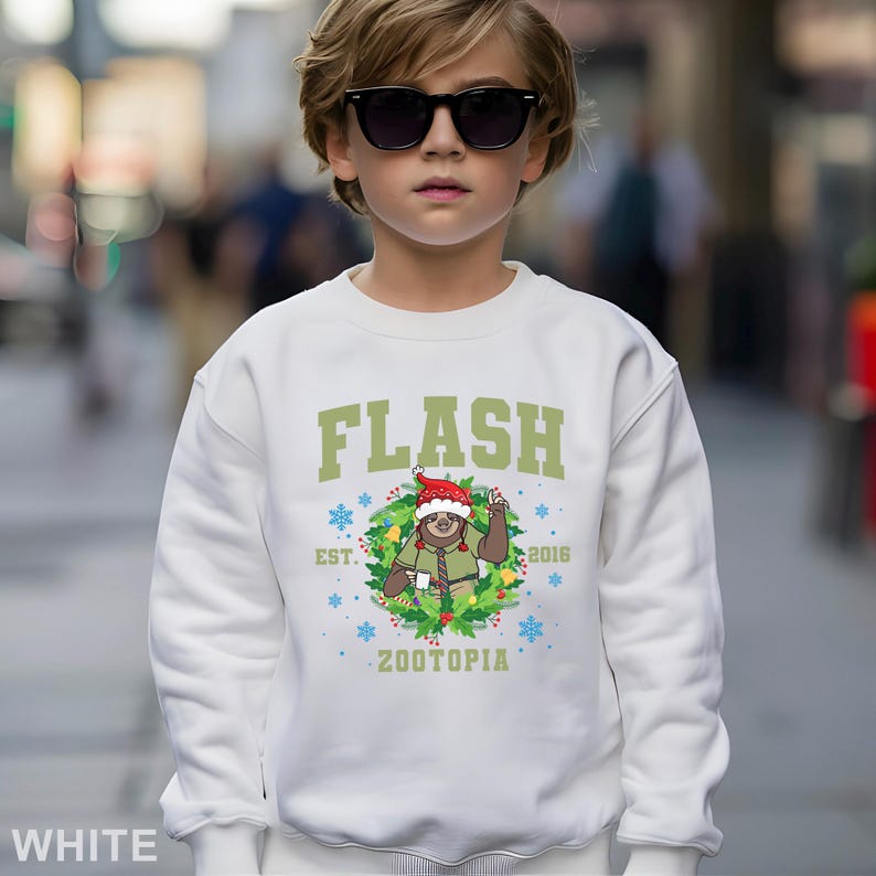 Pu&ograve; includere: Felpa bianca con la scritta "FLASH" in verde. Sotto, un bradipo dei cartoni animati con un cappello da Babbo Natale e una ghirlanda verde. Il testo "EST. 2016" e "ZOOTOPIA" sono stampati anche sulla felpa.