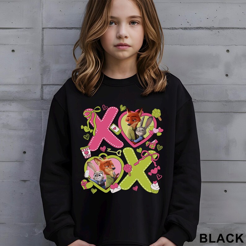 Peut inclure: Sweat-shirt noir avec un motif graphique des personnages de Zootopie, Nick Wilde et Judy Hopps. Le motif comprend des c&oelig;urs roses et verts, les lettres "X" et "O" et d'autres &eacute;l&eacute;ments d&eacute;coratifs. Le mot "BLACK" est imprim&eacute; en bas &agrave; droite.