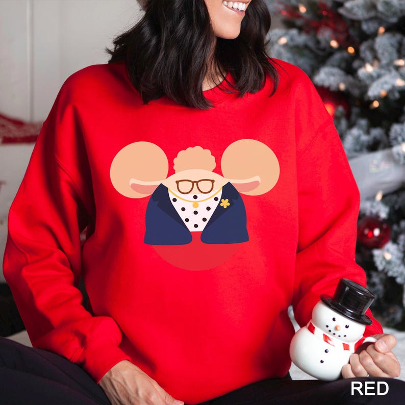 May include: A red sweatshirt featuring a cartoon illustration of a woman wearing glasses, a navy blue blazer, and a polka-dot shirt. The design includes large, tan mouse-ear-like shapes on either side of the woman's head. The word "RED" is printed in the bottom right corner.
