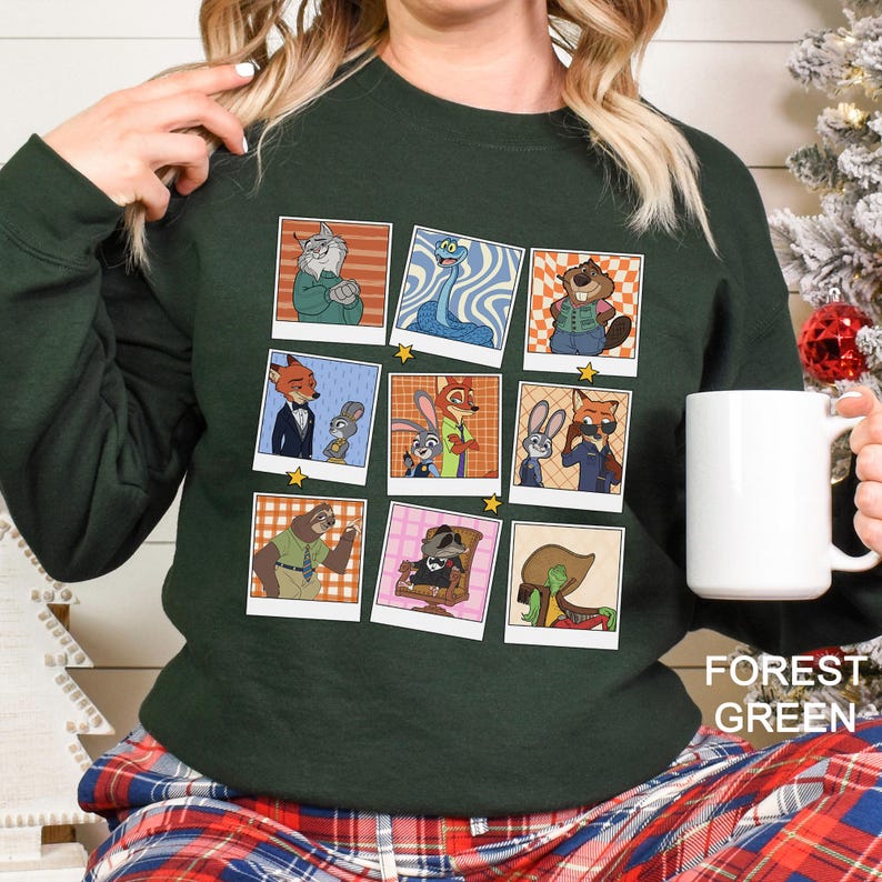 May include: Forest green sweatshirt featuring a grid of cartoon character polaroid-style images. The images include various anthropomorphic animals in different outfits and poses. A white mug is held in the right hand.