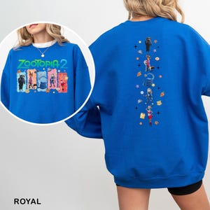 K&ouml;nnte beinhalten: K&ouml;nigsblaues Sweatshirt mit dem Text "ZOOTOPIA 2" und Cartoon-Figuren auf der Vorderseite. Die R&uuml;ckseite hat ein vertikales Design mit Cartoon-Figuren und Sternen. Das Sweatshirt ist aus weichem Material.