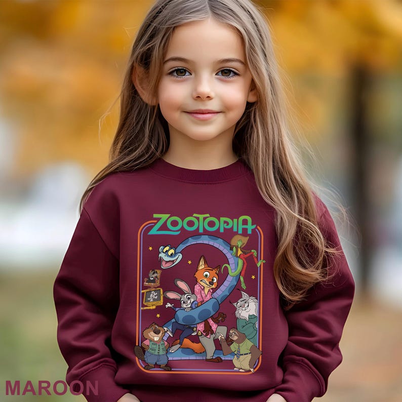 May include: Maroon sweatshirt featuring the word "Zootopia" and cartoon characters. The design includes a blue snake, a fox, a rabbit, and other animal characters. The word "MAROON" is printed at the bottom.