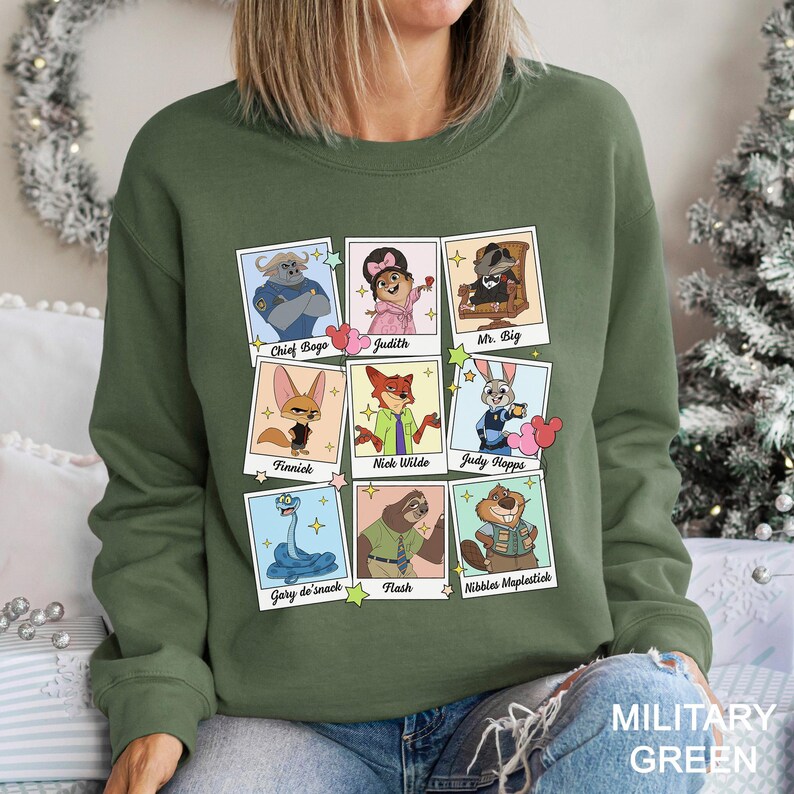 Pu&ograve; includere: Una felpa verde militare con una griglia di ritratti di personaggi dei cartoni animati. Ogni ritratto &egrave; incorniciato ed etichettato con nomi come "Chief Bogo", "Judy Hopps" e "Nick Wilde". Il testo "MILITARY GREEN" &egrave; stampato in basso a destra.