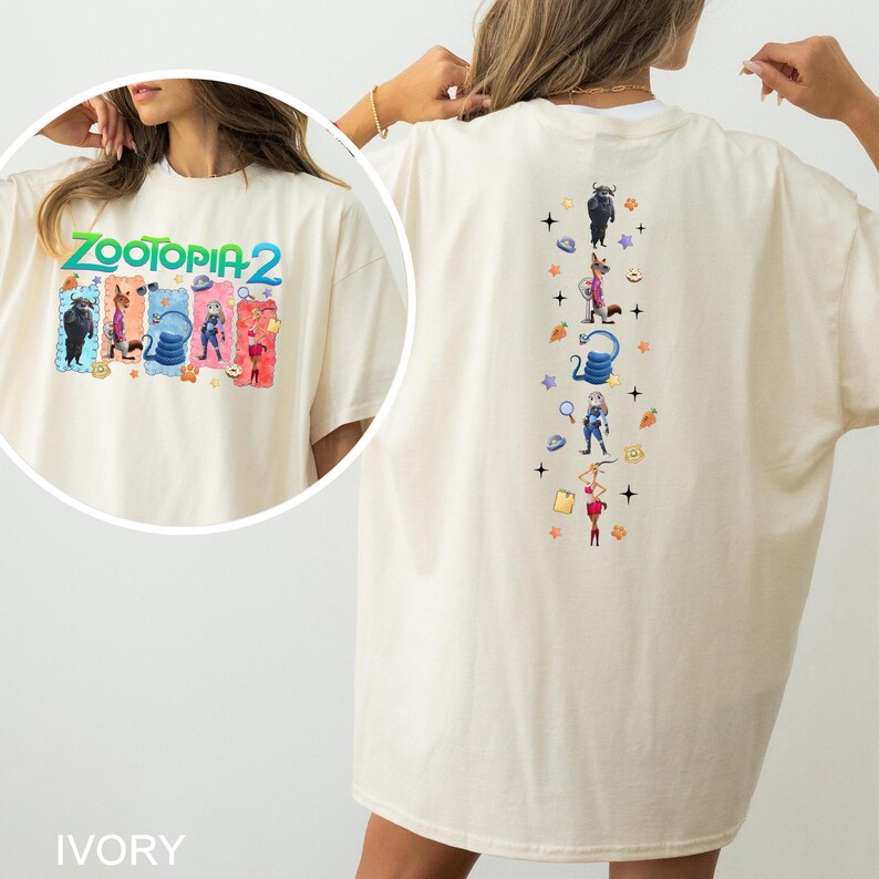 Op de afbeelding: Ivoor kleurig T-shirt met de tekst "Zootopia 2" en kleurrijke cartoonfiguren op de voorkant. De achterkant heeft een verticaal ontwerp met cartoonfiguren en sterren.
