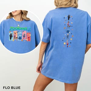 Op de afbeelding: Flo blauw T-shirt met een Zootopia 2 afbeelding op de voor- en achterkant. De afbeelding op de voorkant bevat de tekst "Zootopia 2" en personages. De afbeelding op de achterkant heeft een verticale rangschikking van personages en iconen.