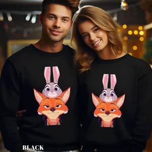 May include: Black sweatshirts featuring a cartoon design of a fox with an orange face and a gray bunny on top. The sweatshirts have long sleeves and a crew neck. The word "BLACK" is printed at the bottom.