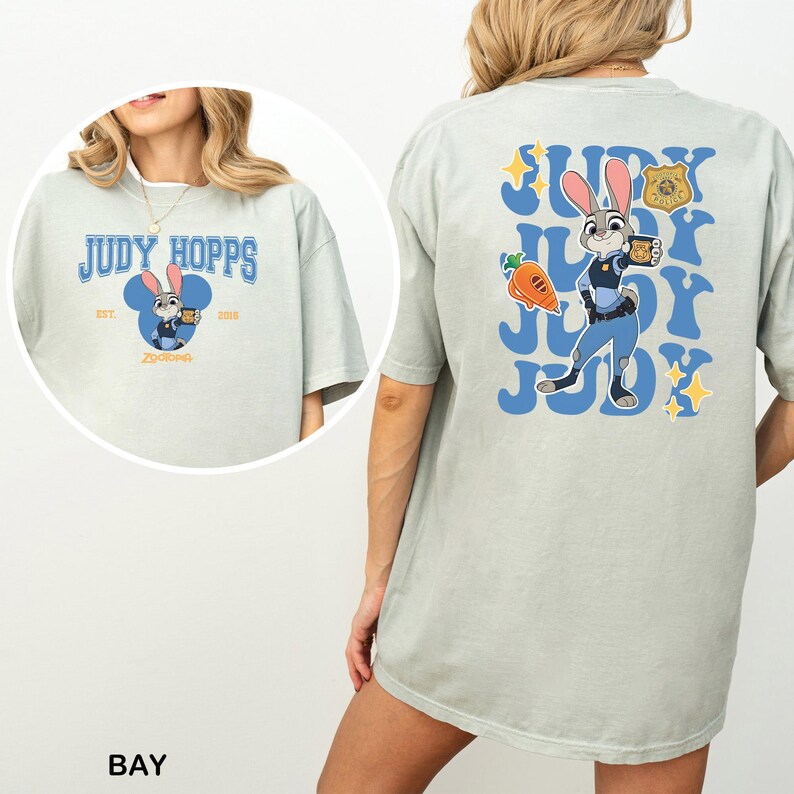 Op de afbeelding: Een licht saliegroen t-shirt met een afbeelding van Judy Hopps uit Zootopia. De voorkant toont de tekst Judy Hopps en Est. 2016. De achterkant toont een grote afbeelding van Judy Hopps, een wortel, een politiebadge en de tekst Judy.