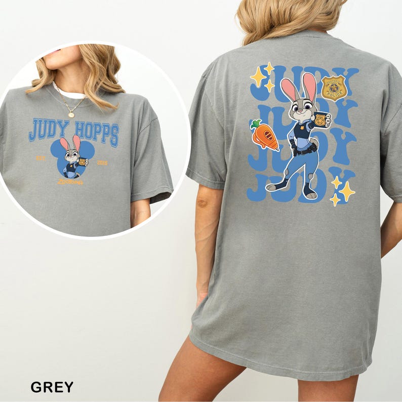 Op de afbeelding: Een grijs t-shirt met een afbeelding van Judy Hopps op de achterkant en een kleinere versie op de voorkant. Het ontwerp op de achterkant bevat het personage, een wortel, een politiebadge en de tekst Judy herhaald in het blauw. De voorkant toont Judy Hopps in een blauw muizenoorsilhouet met de tekst Judy Hopps.