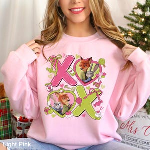Peut inclure: Sweat-shirt rose clair avec un motif graphique repr&eacute;sentant les lettres "XO" et des images d'un renard et d'un lapin &agrave; l'int&eacute;rieur de coeurs. Le motif comprend de petits coeurs, des noeuds et un cupcake. Le sweat-shirt est de couleur rose clair.