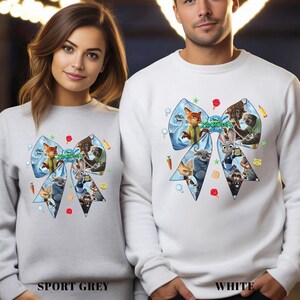 May include: Sport grey and white sweatshirts featuring a large bow design with characters from the animated film "Zootopia." The bow is light blue with various characters and the film's title. The sweatshirts are long-sleeved.