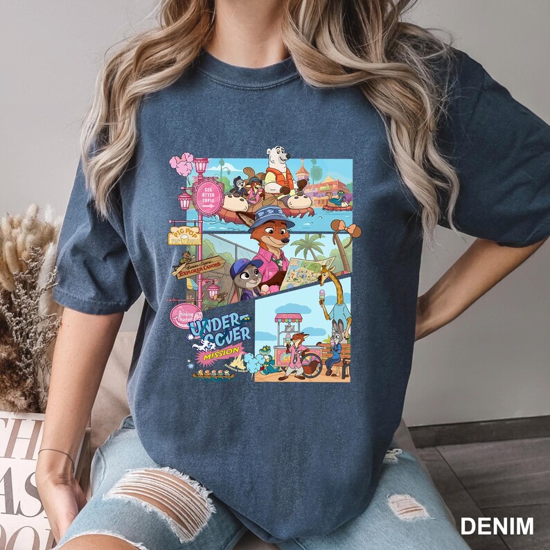 May include: A dark blue short-sleeve t-shirt featuring a multi-panel graphic print of animated animal characters in a theme park setting. The design includes the text "UNDERCOVER MISSION" and various scenes of foxes, rabbits, and other creatures enjoying rides and snacks.