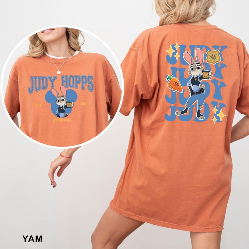 Op de afbeelding: Een oranje t-shirt met Judy Hopps uit Zootropolis. De voorkant toont de tekst Judy Hopps, een blauw Mickey-vormig silhouet en het personage. De achterkant toont een grote afbeelding van Judy Hopps, een wortel, een politiebadge en sterren.