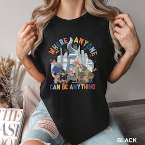 May include: Black t-shirt with a colorful graphic featuring cartoon animal characters and the text "WHERE ANYONE CAN BE ANYTHING". The design includes a cityscape and various animal figures.