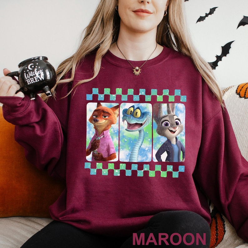 May include: Maroon sweatshirt featuring three cartoon characters in a framed design. The characters include a fox in a pink shirt, a blue snake, and a rabbit in a blue jacket. The word "MAROON" is printed at the bottom.