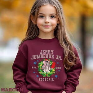 Pu&ograve; includere: Felpa bordeaux con la scritta "JERRY JUMBEAUX JR." sopra una grafica di un elefante e un ghiacciolo, circondati da una ghirlanda. Viene visualizzato anche il testo "EST. 2016 ZOOTOPIA". La parola "MAROON" &egrave; in basso.
