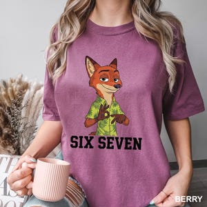 May include: Berry-coloured t-shirt featuring a cartoon fox character in a green Hawaiian shirt, gesturing with his hands. The text "SIX SEVEN" is printed in black below the character. The shirt is a comfortable fit.