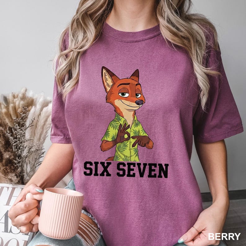 May include: Berry-coloured t-shirt featuring a cartoon fox character in a green Hawaiian shirt, gesturing with his hands. The text "SIX SEVEN" is printed in black below the character. The shirt is a comfortable fit.