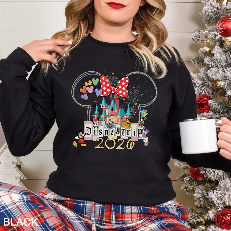 Puede incluir: Sudadera negra con un dise&ntilde;o colorido de Disney Trip 2020. El dise&ntilde;o incluye un castillo, Mickey Mouse, Minnie Mouse y otros personajes de Disney. Un gran lazo rojo con lunares est&aacute; en la parte superior del dise&ntilde;o.