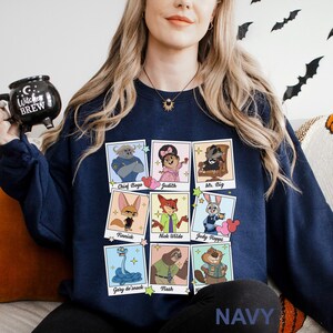 Pu&ograve; includere: Felpa blu navy con un collage di ritratti di personaggi dei cartoni animati. I ritratti includono Chief Bogo, Judith, Mr. Big, Finnick, Nick Wilde, Judy Hopps, Gary de'snack e Flash. La parola "NAVY" &egrave; stampata in basso.