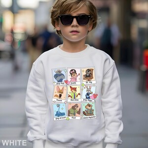 Pu&ograve; includere: Una felpa bianca con una griglia di ritratti di personaggi dei cartoni animati. Ogni ritratto &egrave; in una cornice in stile polaroid. I personaggi includono Chief Bogo, Judith, Mr. Big, Finnick, Nick Wilde, Judy Hopps, Gary de Snack, Flash e Nibbles Maplestick. La parola "WHITE" &egrave; in basso.