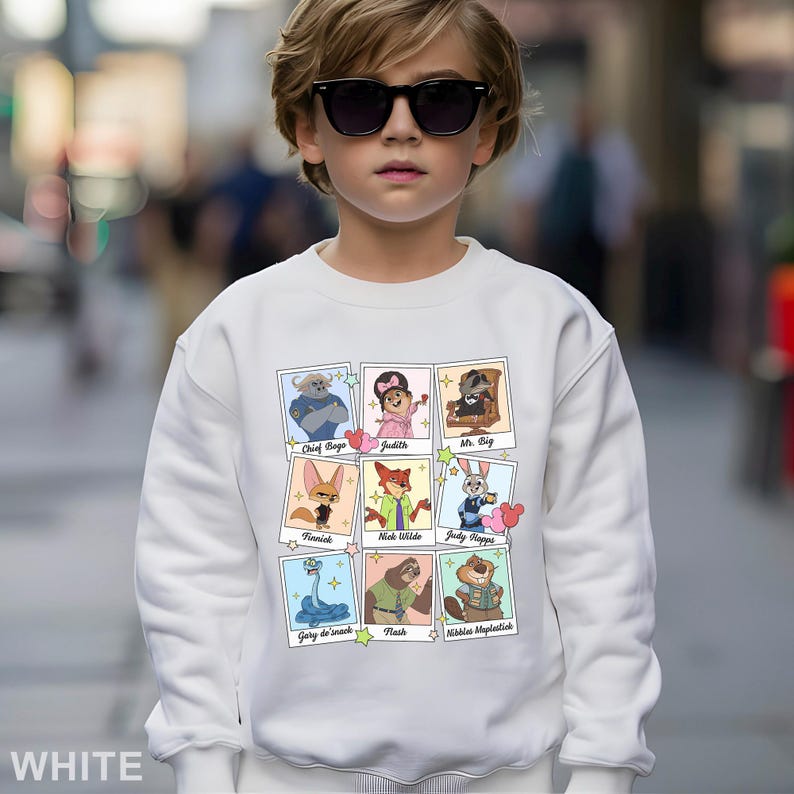 Pu&ograve; includere: Una felpa bianca con una griglia di ritratti di personaggi dei cartoni animati. Ogni ritratto &egrave; in una cornice in stile polaroid. I personaggi includono Chief Bogo, Judith, Mr. Big, Finnick, Nick Wilde, Judy Hopps, Gary de Snack, Flash e Nibbles Maplestick. La parola "WHITE" &egrave; in basso.