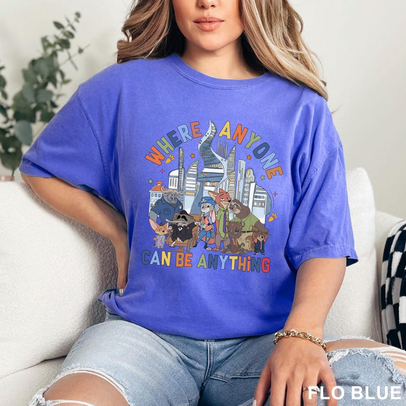 May include: A blue t-shirt with the text "WHERE ANYONE CAN BE ANYTHING" and a cartoon graphic of animal characters and a city skyline. The shirt is a solid blue color.