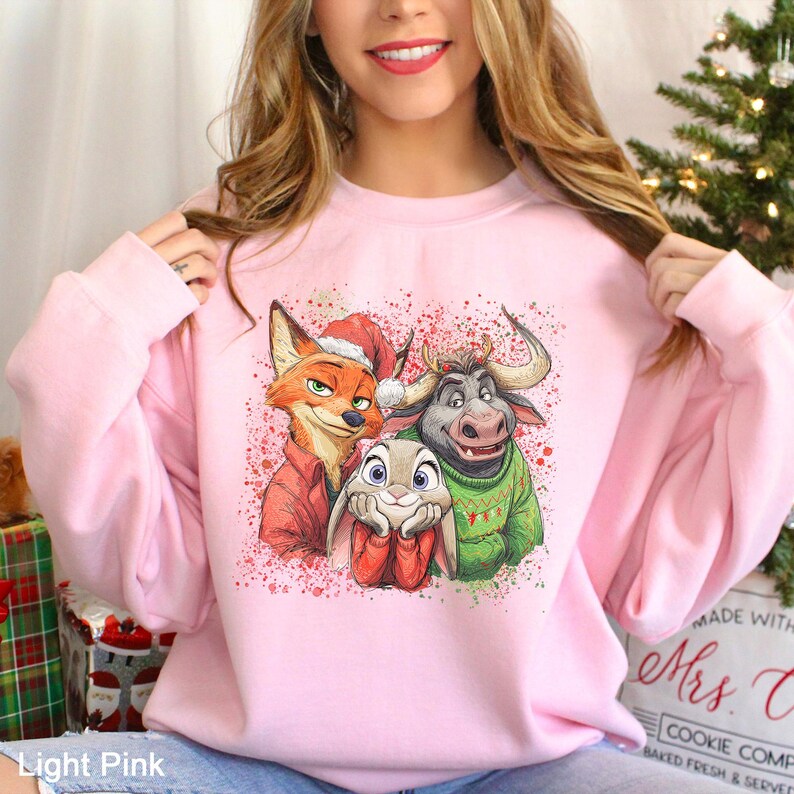 May include: Light pink sweatshirt featuring a graphic of a fox, bunny, and bull in Christmas attire. The fox wears a Santa hat and red coat, the bunny has red mittens, and the bull wears a green sweater. The sweatshirt has a crew neck.