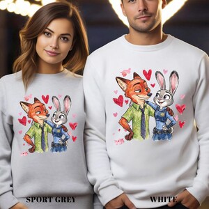 Pu&ograve; includere: Felpe grigio sport e bianche con un'illustrazione ad acquerello di Nick Wilde e Judy Hopps di Zootropolis, circondate da cuori rossi. Le felpe hanno le parole "SPORT GREY" e "WHITE" stampate in basso.