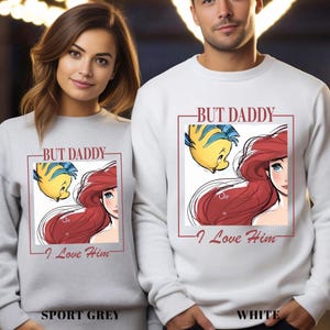 May include: Sport grey and white sweatshirts featuring Ariel and Flounder from The Little Mermaid, with the text "BUT DADDY - I Love Him" in a red box. The sport grey sweatshirt is labelled "SPORT GREY" and the white sweatshirt is labelled "WHITE".