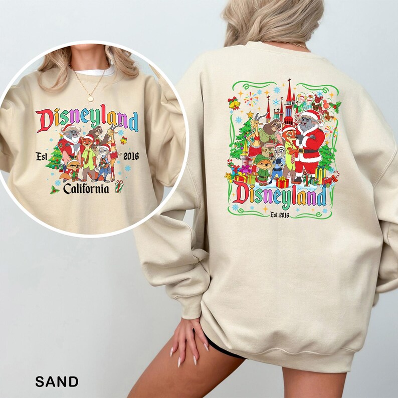May include: Sand-colored sweatshirt with a Disneyland graphic on the front and back. The front graphic says "Disneyland California Est. 2016" with cartoon characters. The back graphic has a similar design with a castle and Santa.