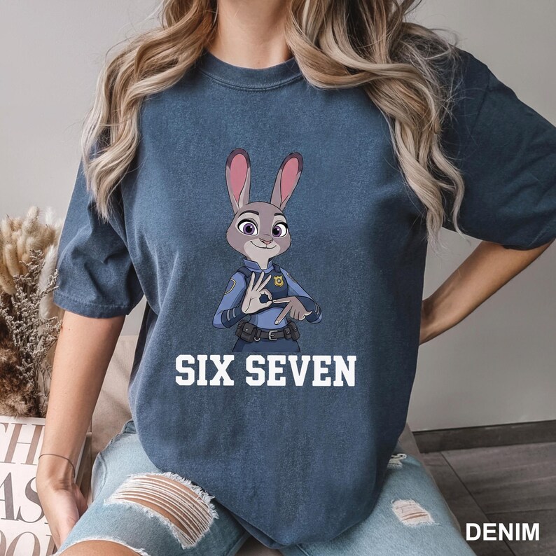 May include: A denim blue t-shirt with a cartoon image of Judy Hopps from Zootopia. The character is in a police uniform and making a hand gesture. The text "SIX SEVEN" is printed in white below the image.