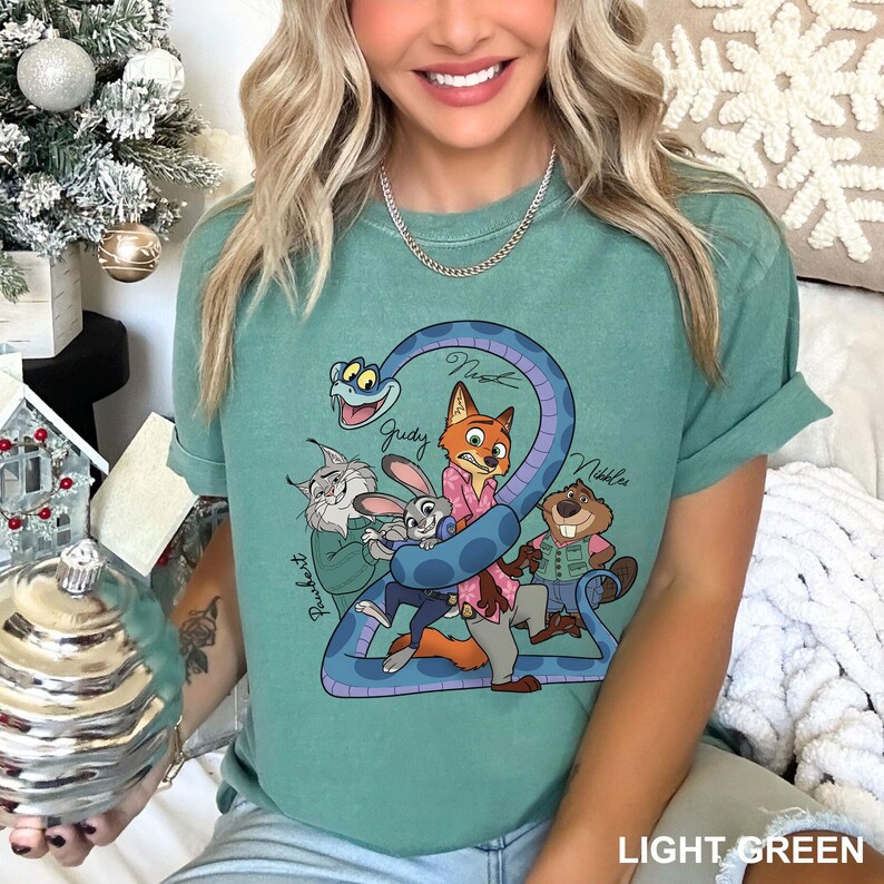 Puede incluir: Camiseta verde claro con una ilustraci&oacute;n de dibujos animados de personajes de animales, incluyendo un zorro, un conejo y un castor, envueltos en una serpiente azul. Los nombres de los personajes est&aacute;n escritos en la camiseta. Las palabras "LIGHT GREEN" est&aacute;n en la parte inferior.