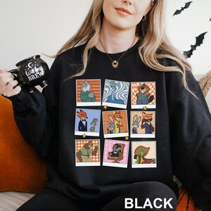 May include: Black sweatshirt featuring a grid of cartoon character portraits in retro style. The portraits are in colorful frames with a variety of animal characters. The word "BLACK" is printed at the bottom of the sweatshirt.