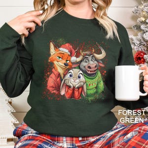 May include: Forest green sweatshirt featuring a graphic of three cartoon characters in holiday attire. The characters include a fox in a Santa hat, a bunny, and a bull. Red and green accents are scattered around the image.
